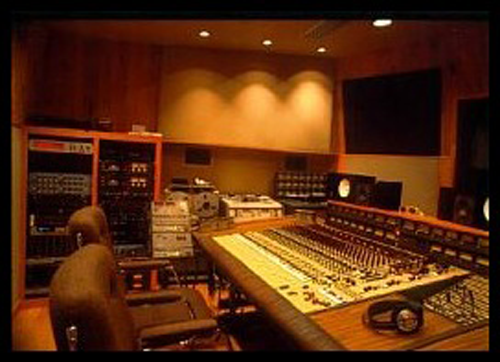 The producer’s side of a recording studio with a wide sound board, two chairs, and different sound equipment